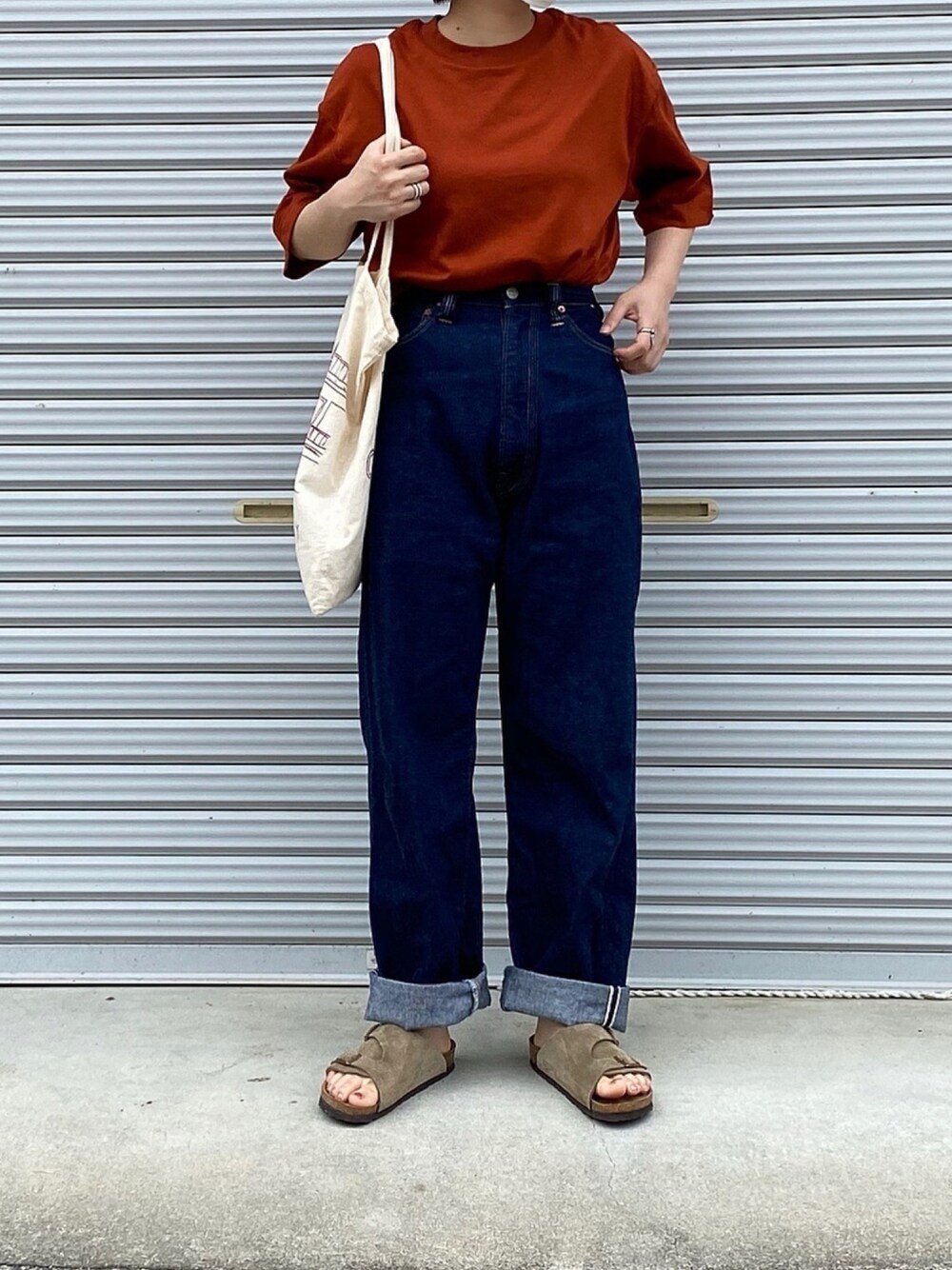 オレンジ系のTシャツ/カットソー、ブルー系のデニムパンツ、ベージュ系のサンダルを着用したレディースの夏コーディネートの1枚目の写真