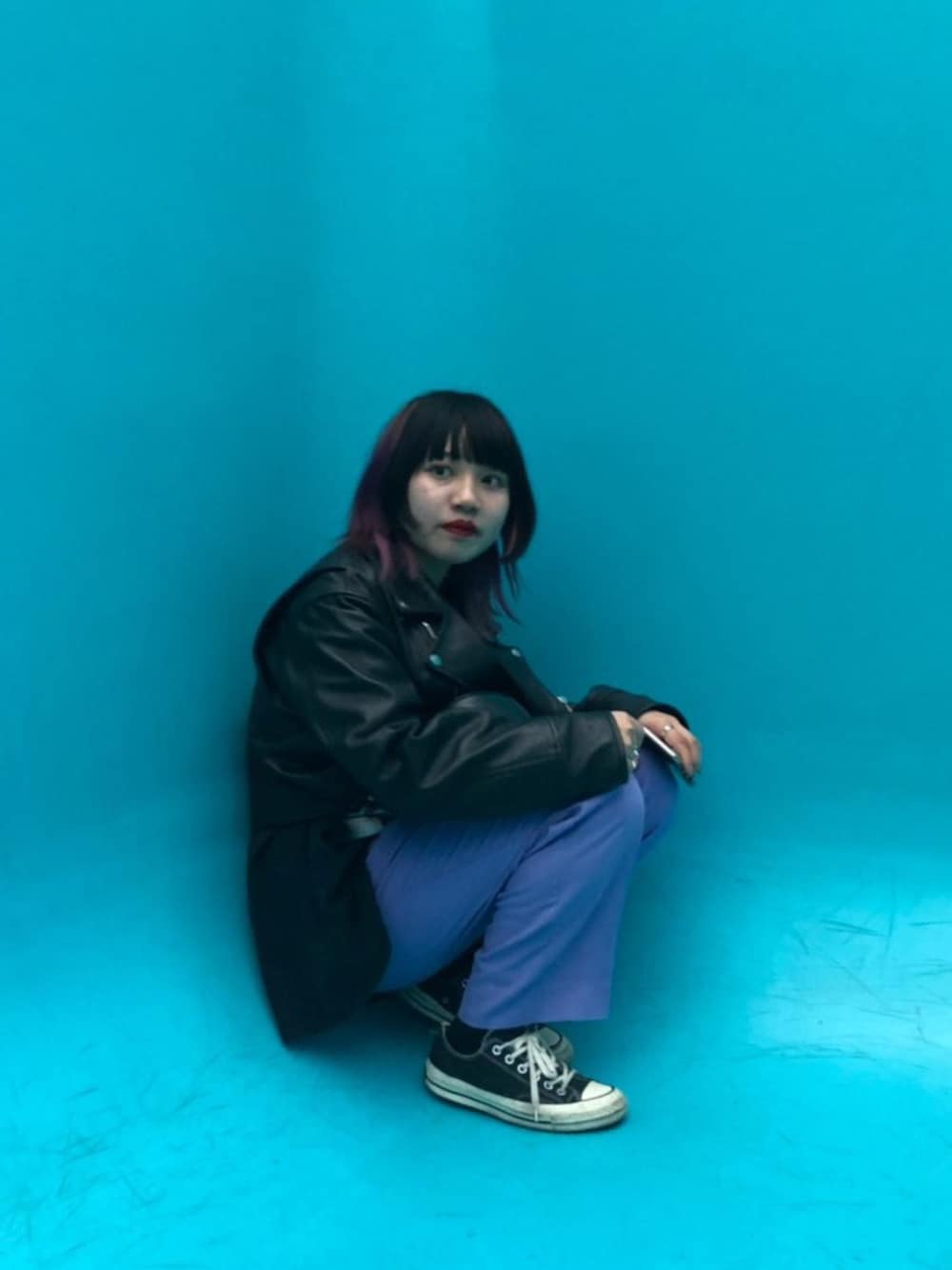 ブラック系のライダースジャケット、パープル系のスラックス、ブラック系のスニーカーを着用したレディースの冬コーディネートの1枚目の写真