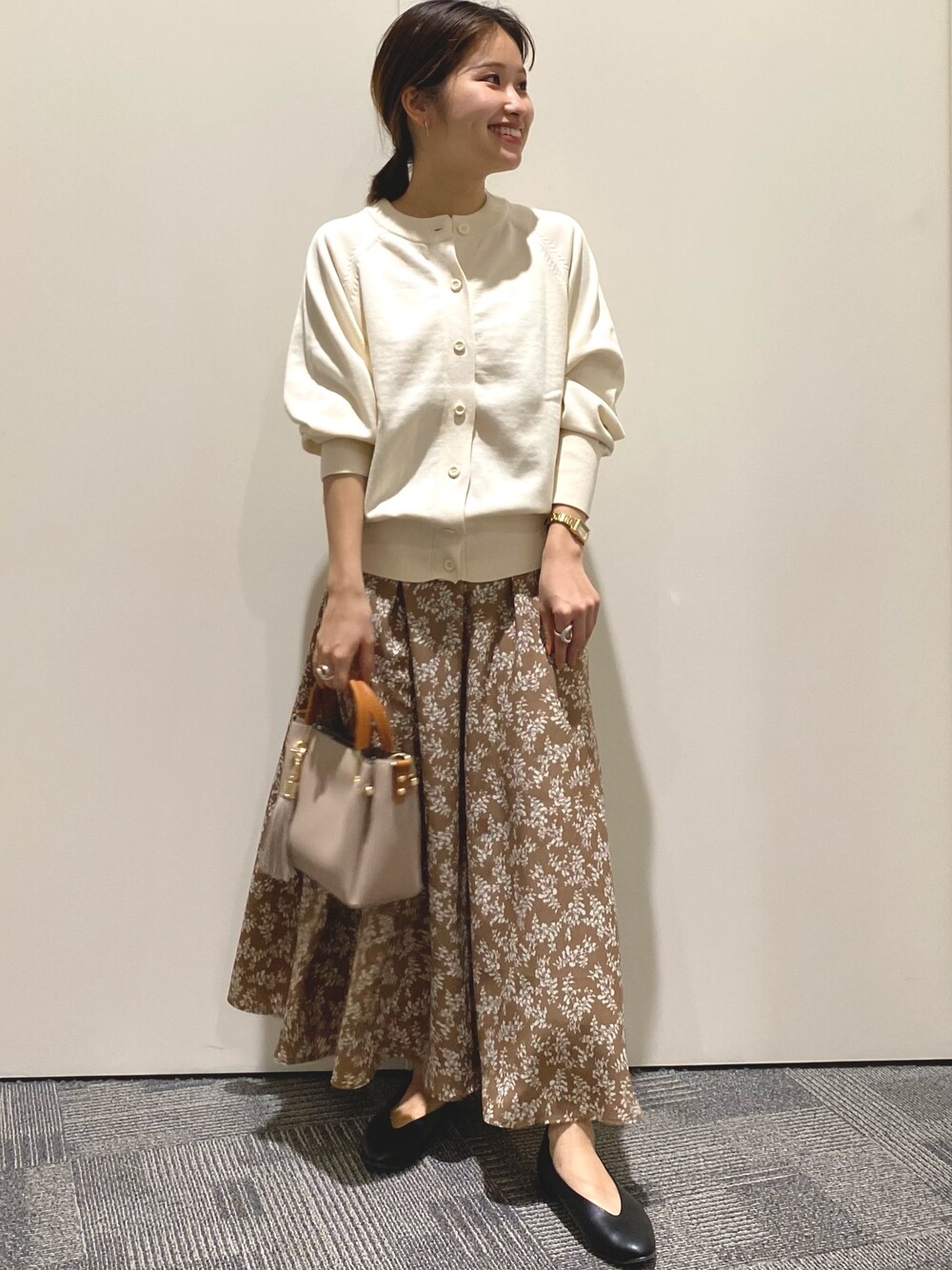 ホワイト系のカーディガン/ボレロ、ブラウン系のスカート、ベージュ系のトートバッグを着用したレディースの春コーディネートの1枚目の写真