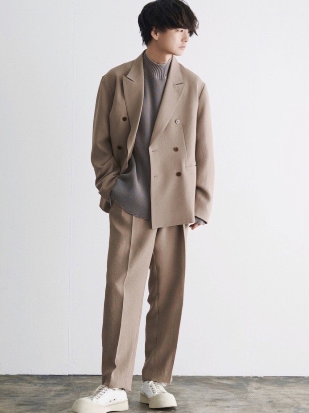 ベージュ系のテーラードジャケット、グレー系のトップス、ベージュ系のスラックスを着用したメンズの春コーディネートの1枚目の写真