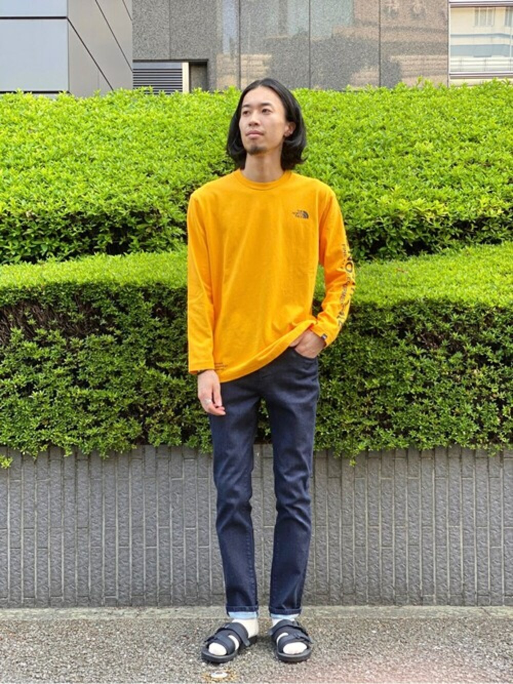 ブルー系のデニムパンツ、ゴールド系のTシャツ/カットソー、ブラック系のサンダルを着用したメンズの秋コーディネートの1枚目の写真