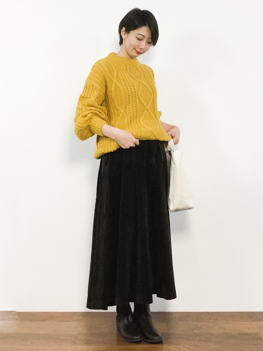 イエロー系のニット/セーター、ブラウン系のスカートを着用したレディースの秋コーディネートの1枚目の写真