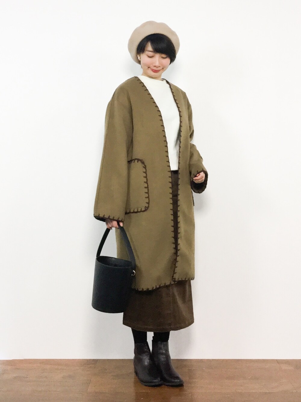 イエロー系のチェスターコート、ブラウン系のスカート、ホワイト系のスウェットを着用したレディースの冬コーディネートの1枚目の写真