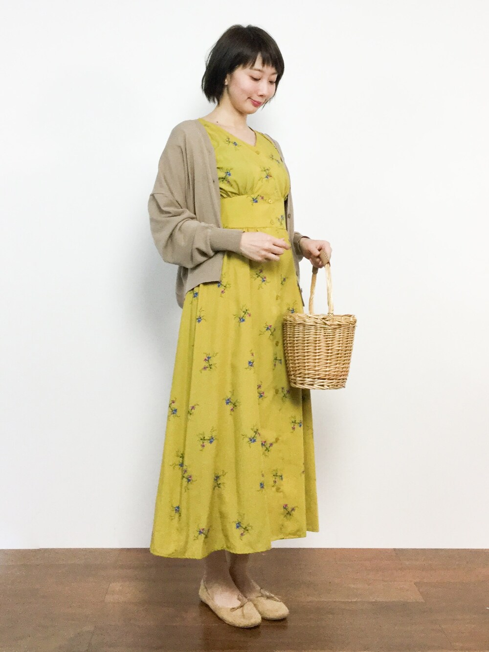 イエロー系のワンピース、ベージュ系のかごバッグ、ブラウン系のカーディガン/ボレロを着用したレディースの春コーディネートの1枚目の写真