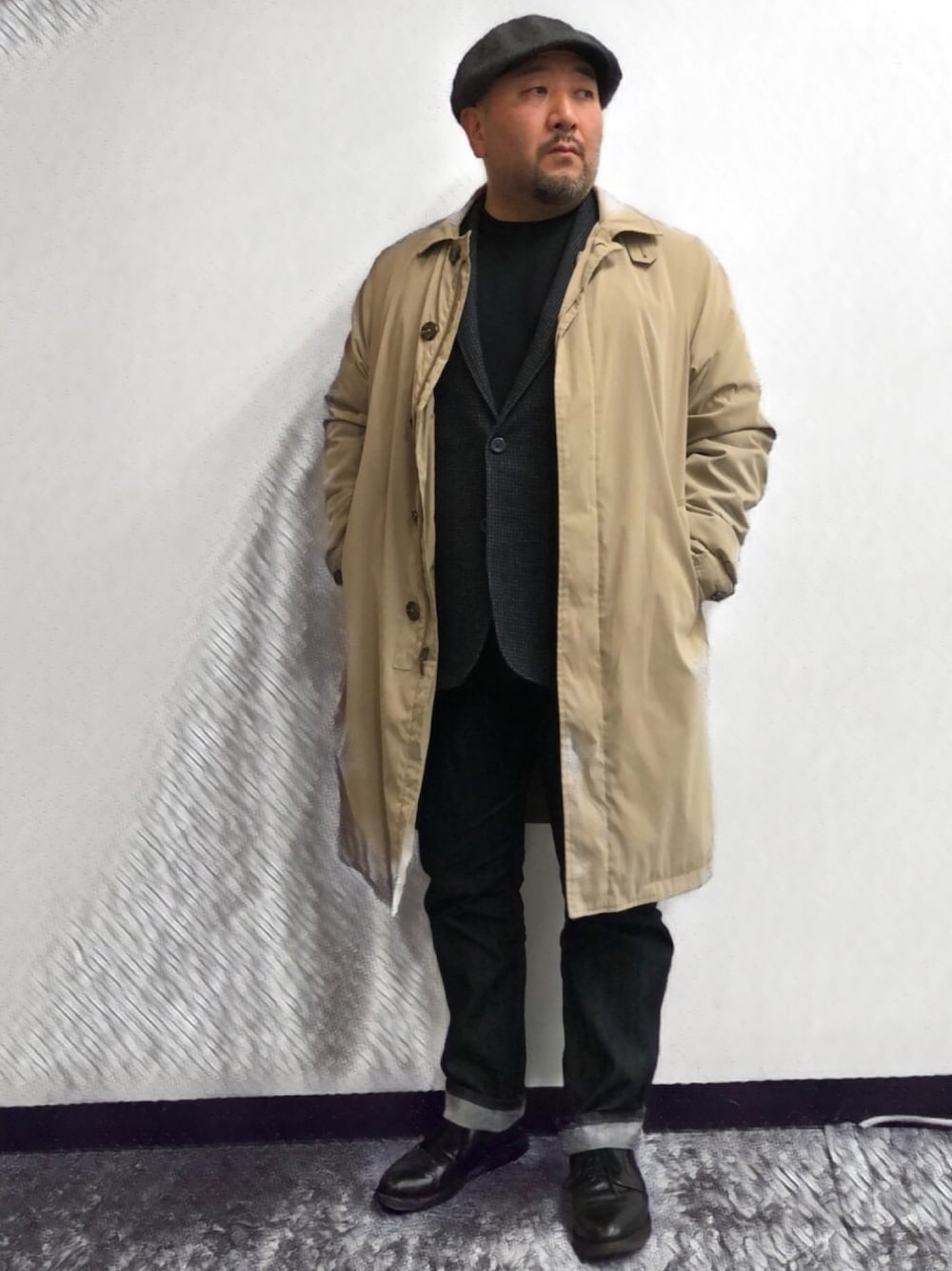 ベージュ系のステンカラーコート、ブラック系のテーラードジャケット、ブラック系のデニムパンツを着用したメンズの冬コーディネートの1枚目の写真