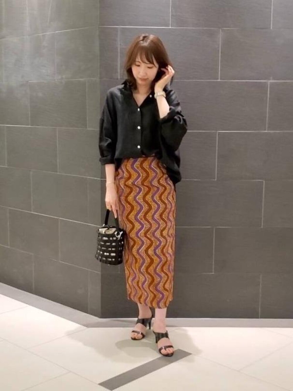 ブラック系のシャツ/ブラウス、オレンジ系のスカート、シルバー系のネックレスを着用したレディースの夏コーディネートの1枚目の写真