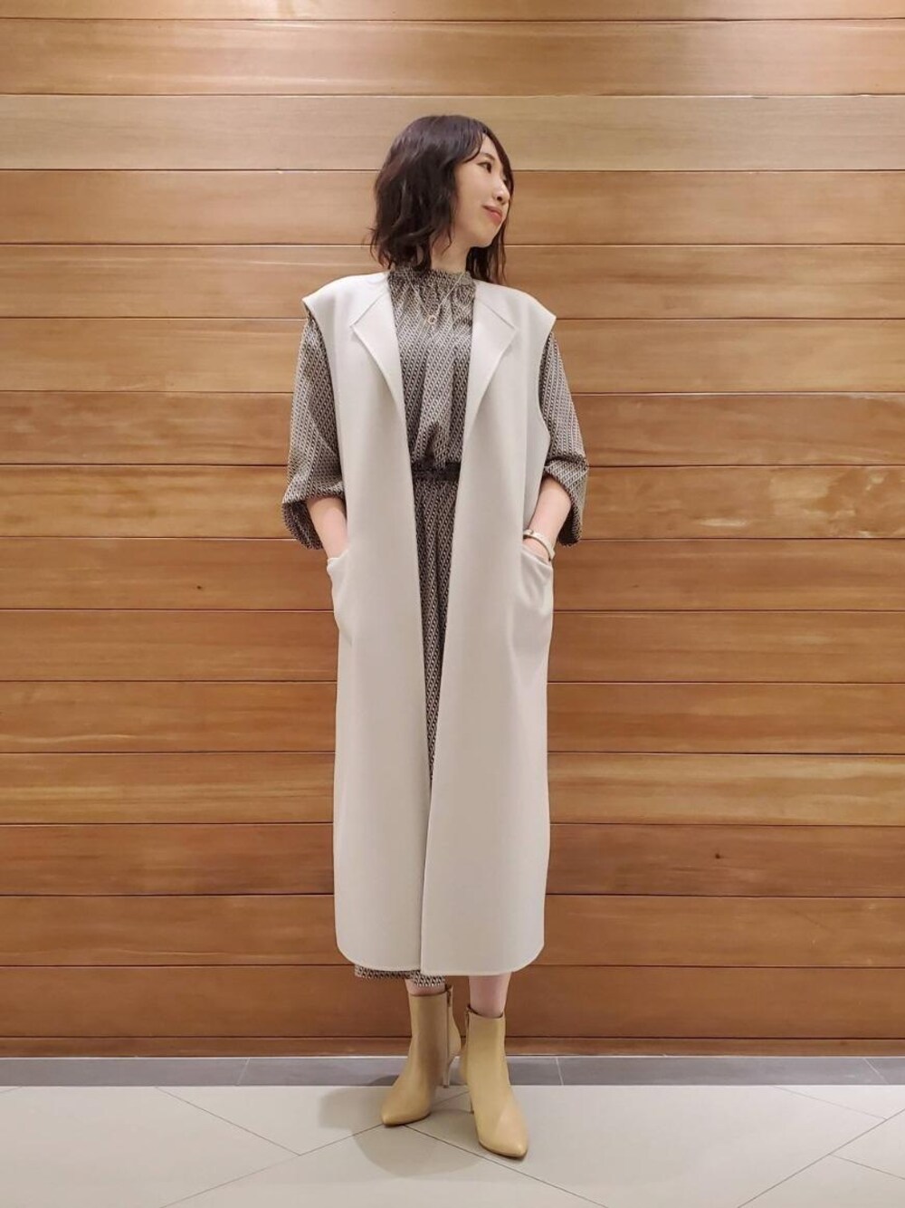 ベージュ系のブーツ、ホワイト系のベスト、グリーン系のワンピースを着用したレディースの秋コーディネートの1枚目の写真