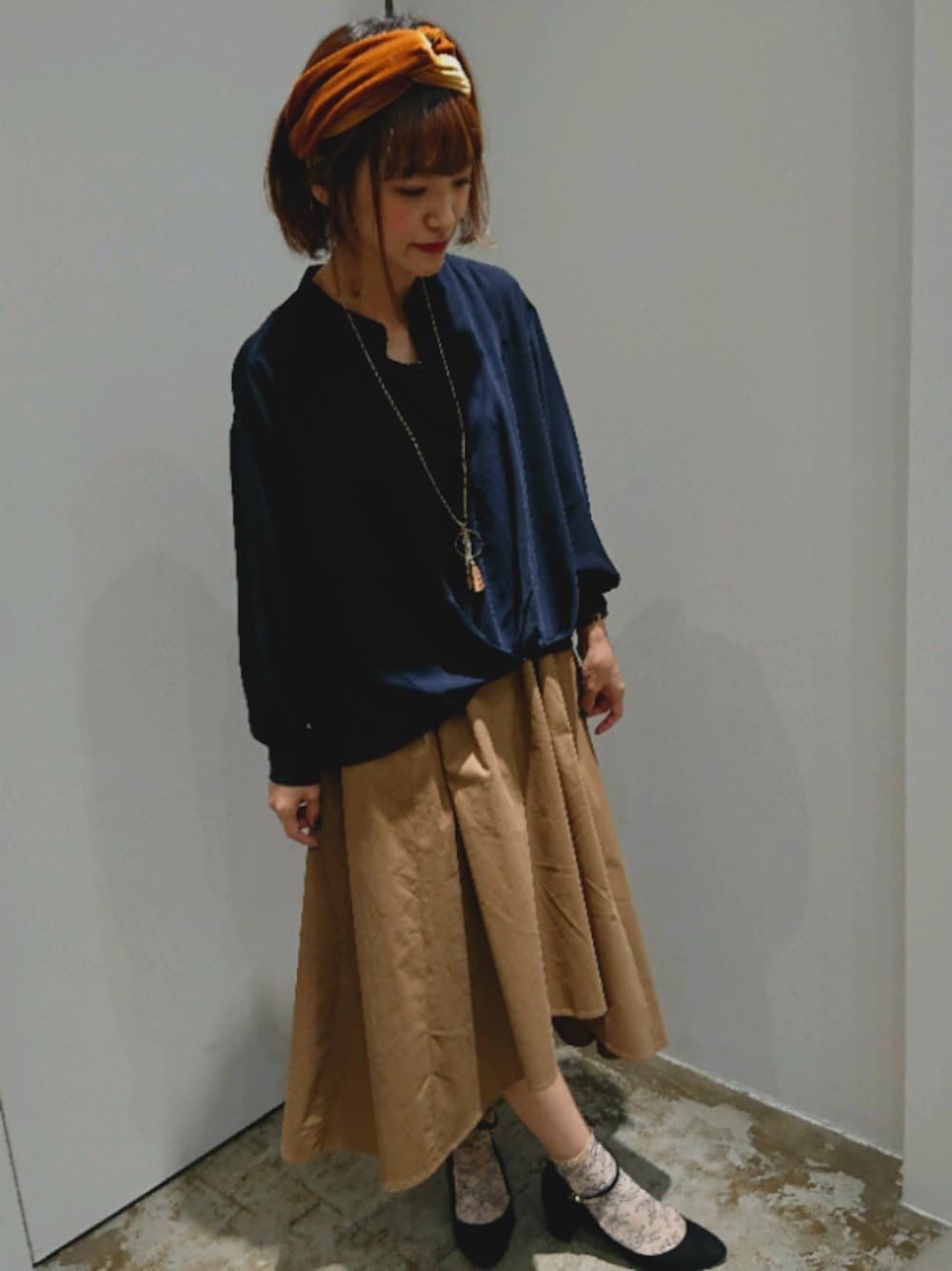 ベージュ系のワンピース、イエロー系のヘアバンド、ブラウン系のネックレスを着用したレディースの秋コーディネートの1枚目の写真