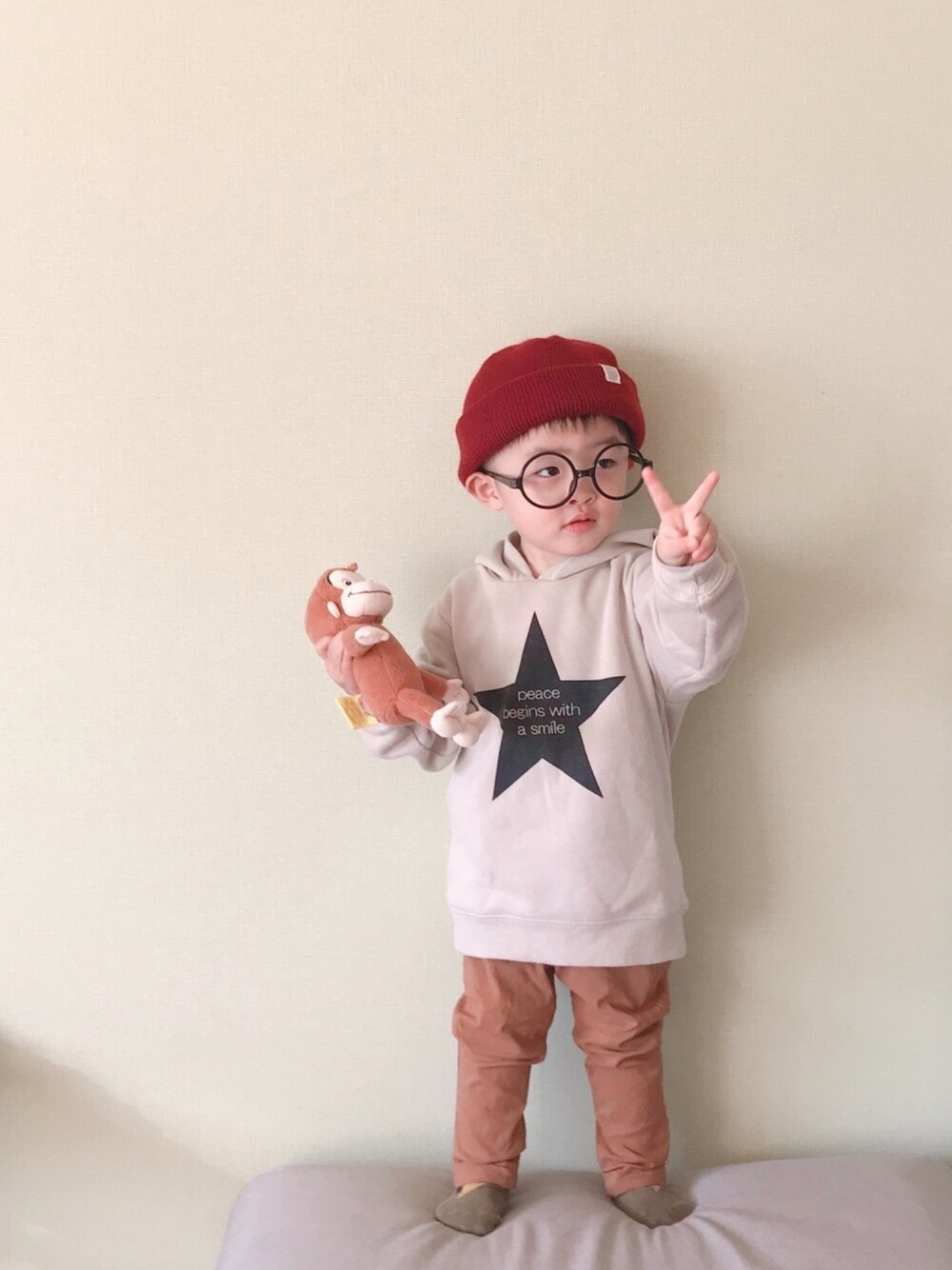 「2歳5ヶ月、おとこのこ、キッズコーデ、パーカー、ブラウンコーデ、シンプル、開き気味のピース✌️、からのやはりおちょけ、おさるのジョージ、めがね」｜「koreaのアイテム（ニットキャップ/ビーニー、レッド系）」を使った、モリコさん（キッズ・80cm）の冬コーディネートの1枚目の写真