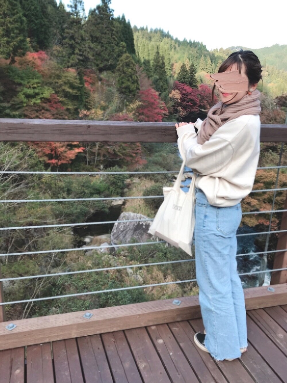 ブルー系のデニムパンツ、ベージュ系のスウェット、ホワイト系のトートバッグを着用したレディースの秋コーディネートの1枚目の写真