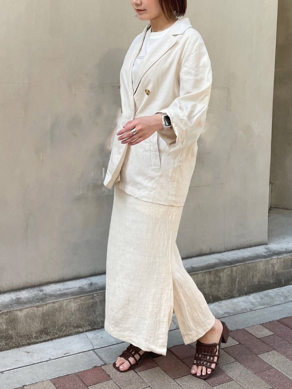ホワイト系のテーラードジャケット、ホワイト系のスカート、ブラウン系のサンダルを着用したレディースの春コーディネートの1枚目の写真