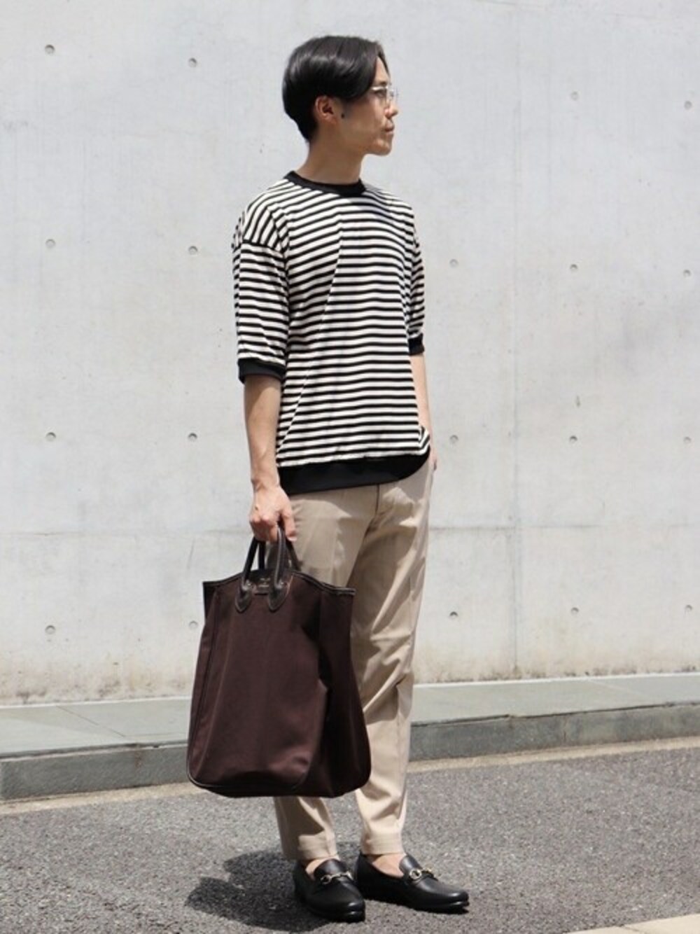 ブラック系のTシャツ/カットソー、ベージュ系のその他パンツ、ブラウン系のトートバッグを着用したメンズの春コーディネートの1枚目の写真