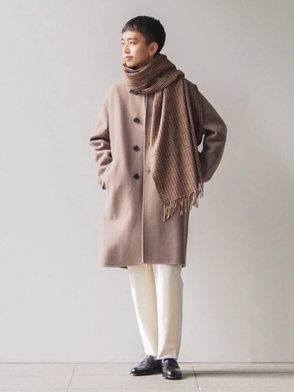 ベージュ系のステンカラーコート、ホワイト系のその他パンツ、ブラック系のローファーを着用したメンズの冬コーディネートの1枚目の写真