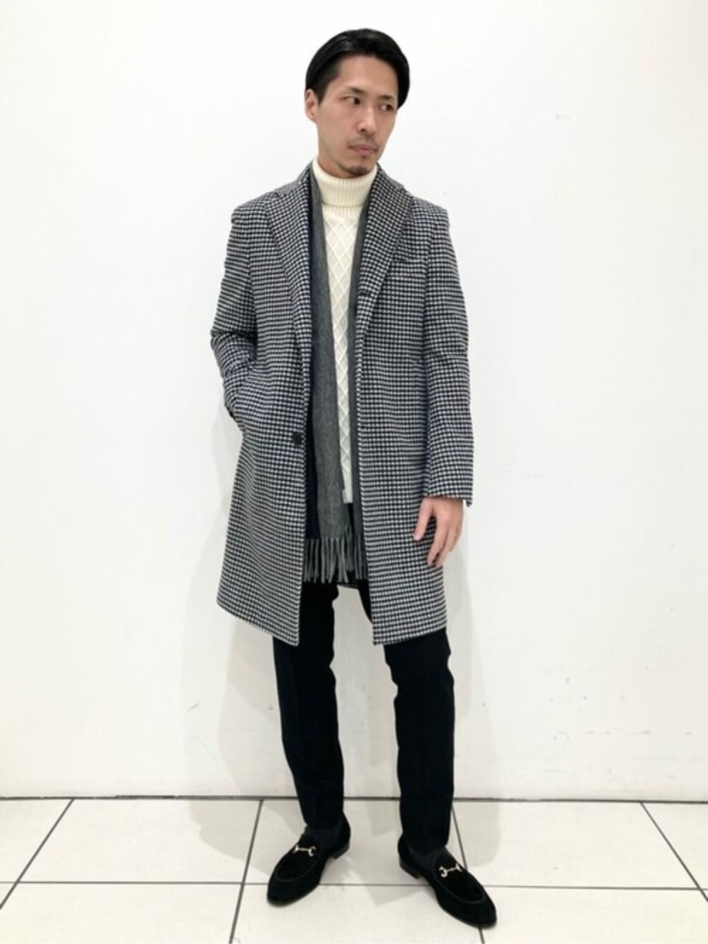 グレー系のチェスターコート、ホワイト系のニット/セーター、ブラック系のその他パンツを着用したメンズの冬コーディネートの1枚目の写真