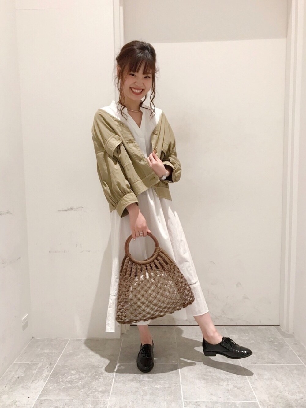 ベージュ系のミリタリージャケット、ブラウン系のかごバッグ、ブラック系のドレスシューズを着用したレディースの夏コーディネートの1枚目の写真