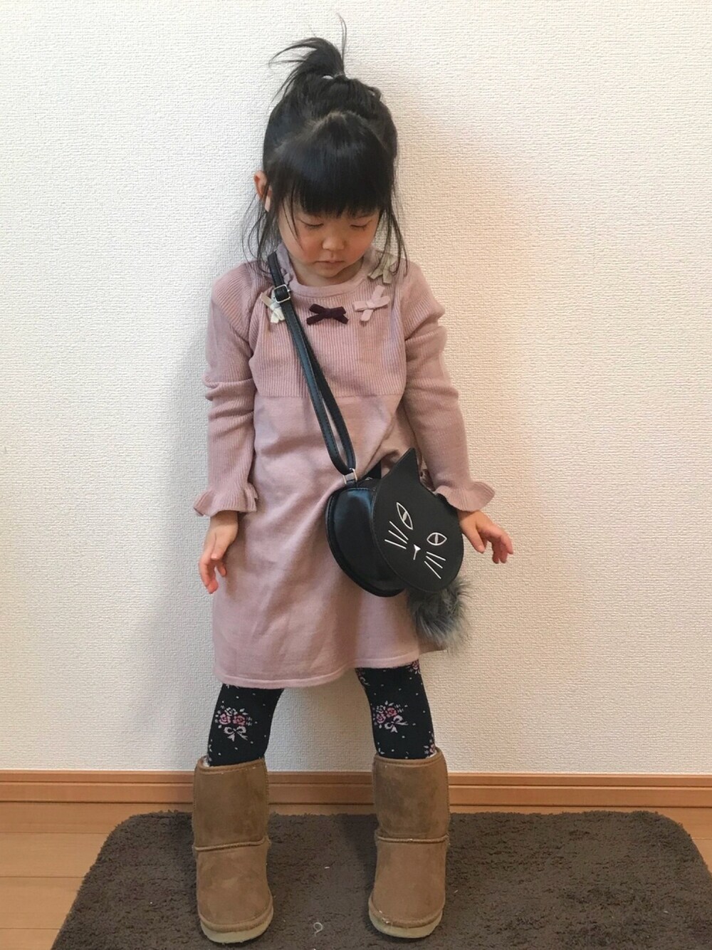 ピンク系のワンピース、ブラック系のショルダーバッグ、ブラウン系のブーツを着用したキッズの冬コーディネートの1枚目の写真