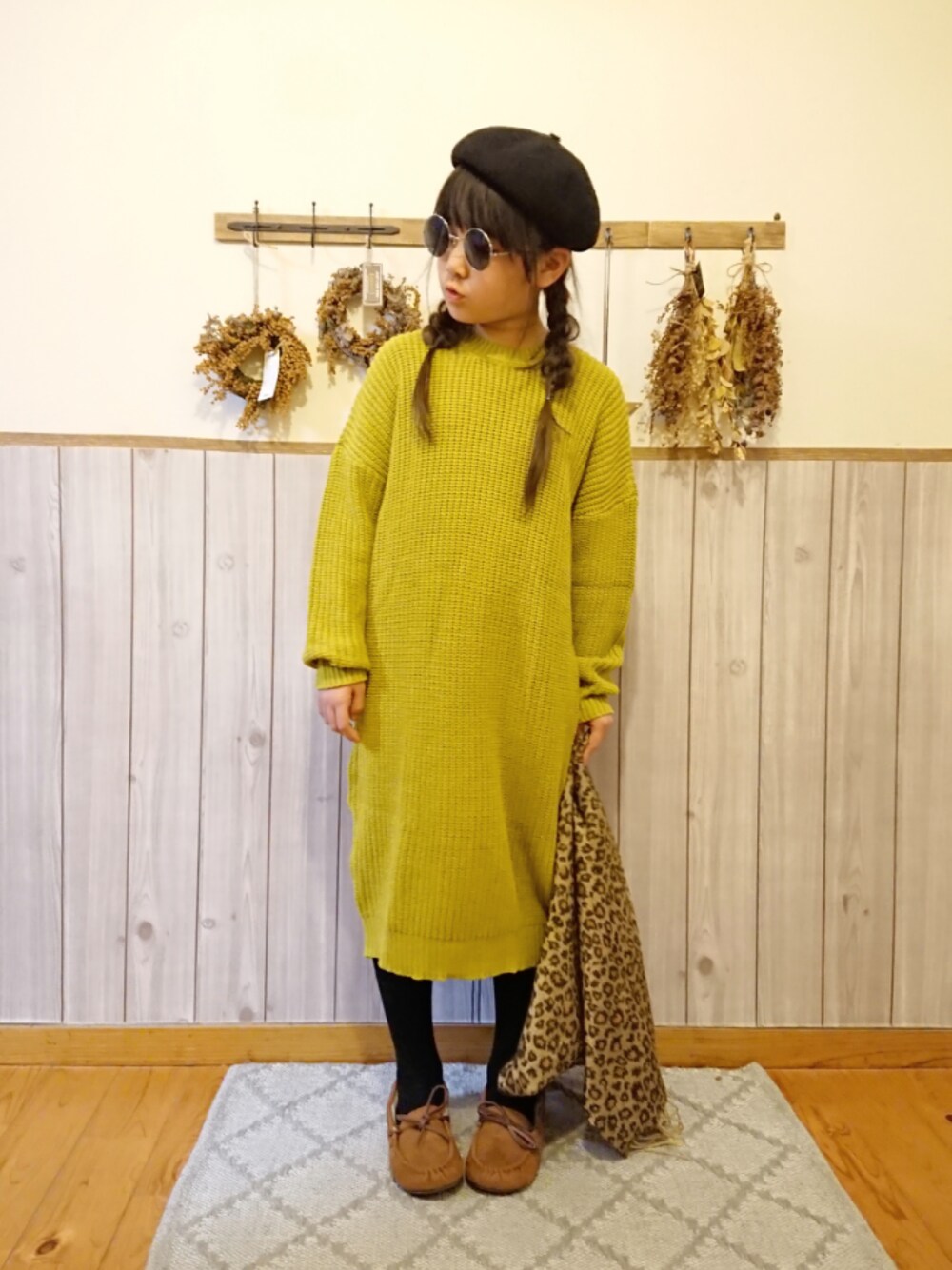 イエロー系のワンピース、ブラウン系のモカシン/デッキシューズ、ブラック系のハンチング/ベレー帽を着用したキッズの冬コーディネートの1枚目の写真