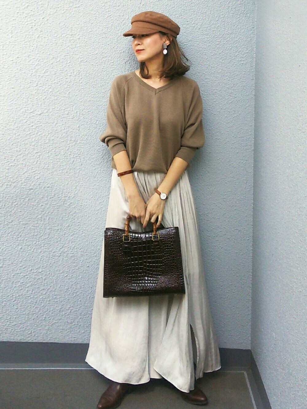 グレー系のスカート、グリーン系のニット/セーター、ブラウン系のアナログ腕時計を着用したレディースの春コーディネートの1枚目の写真