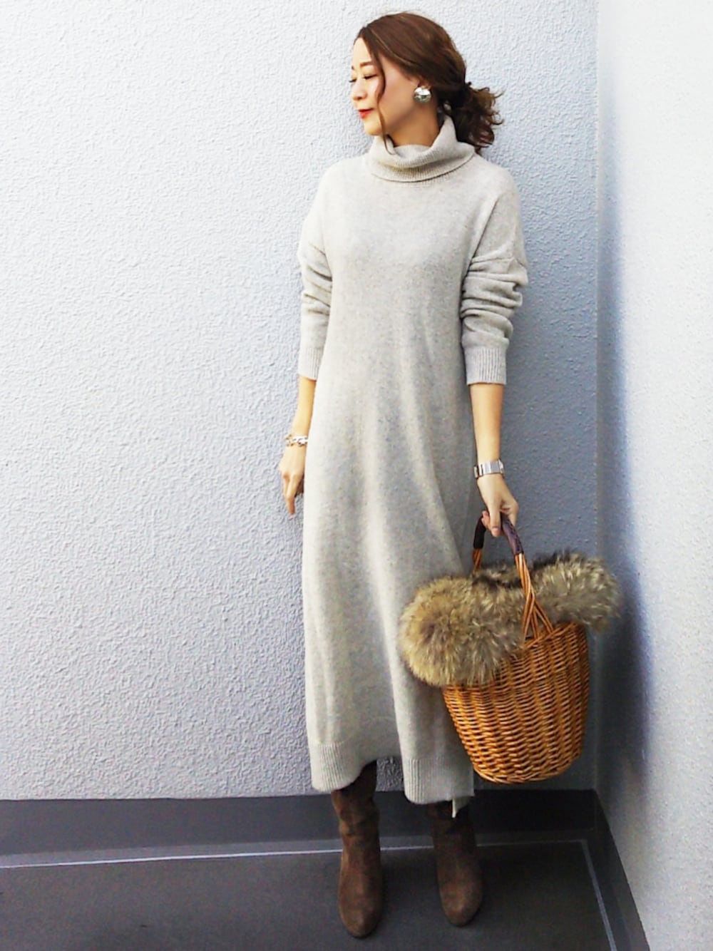 グレー系のワンピース、ベージュ系のかごバッグ、シルバー系のイヤリングを着用したレディースの冬コーディネートの1枚目の写真