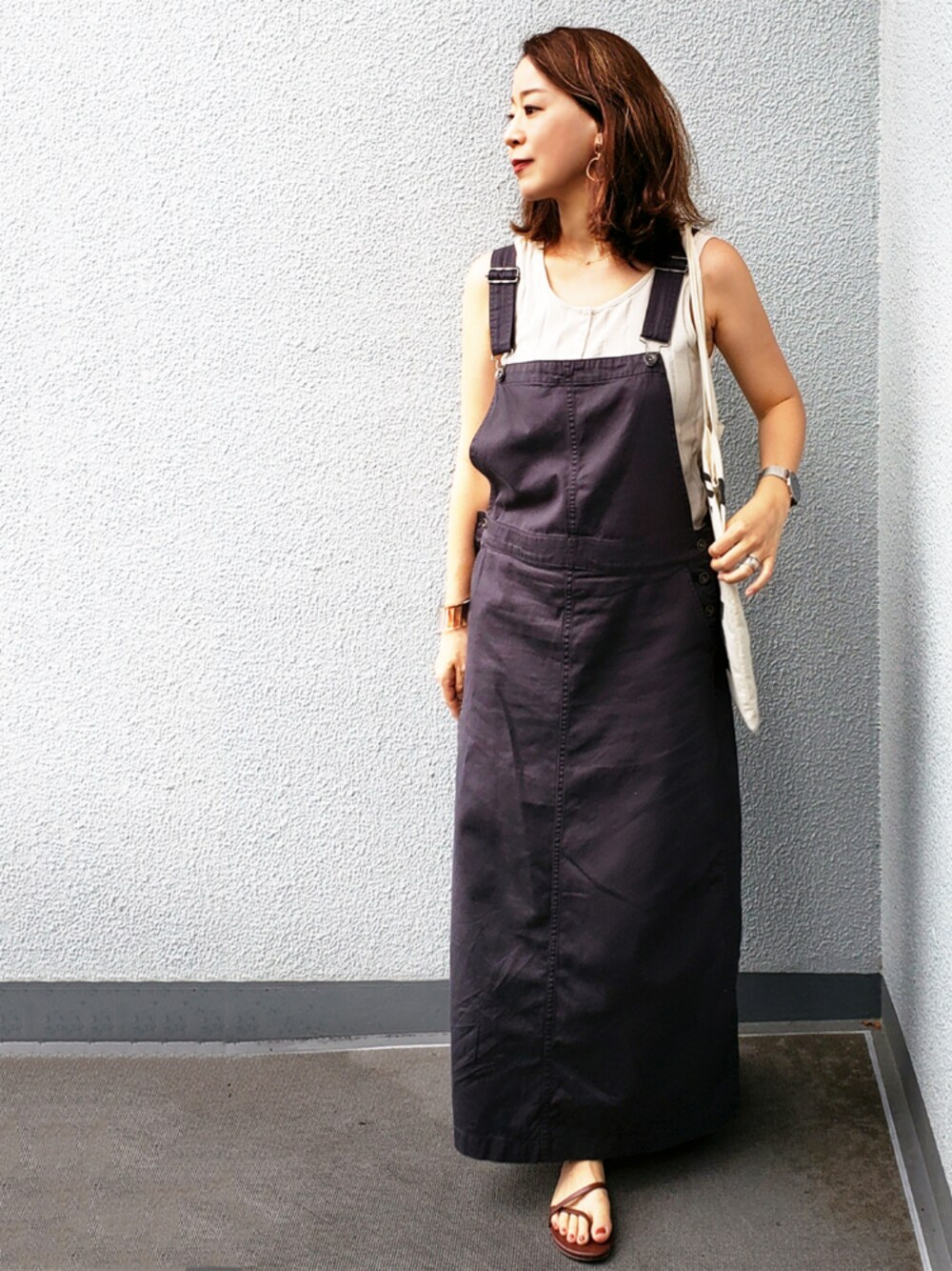 ベージュ系のタンクトップ、ブラック系のサロペット/オーバーオール、ブラウン系のサンダルを着用したレディースの夏コーディネートの1枚目の写真