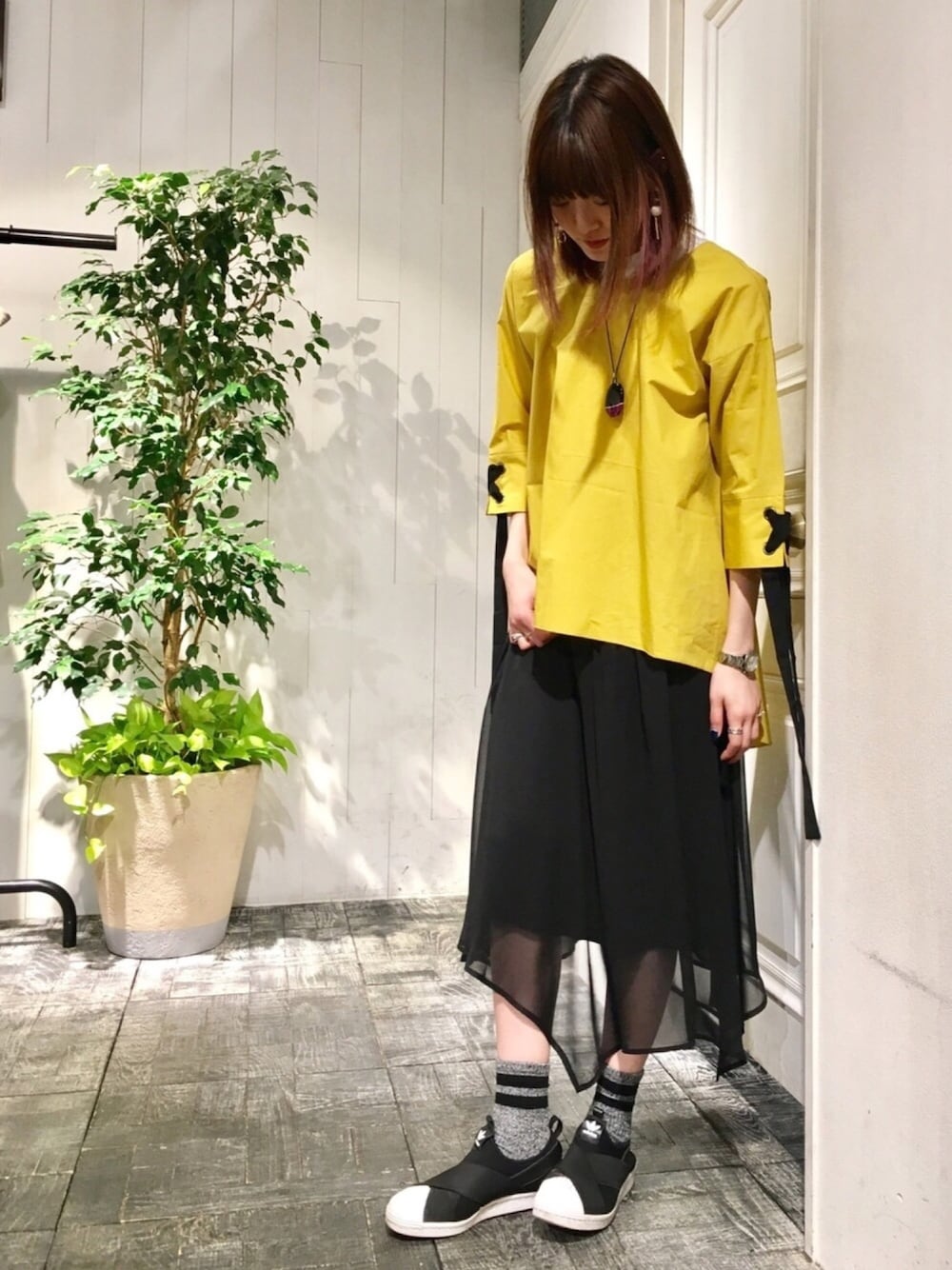 イエロー系のシャツ/ブラウス、ブラック系のスカート、ブラック系のスリッポンを着用したレディースの春コーディネートの1枚目の写真