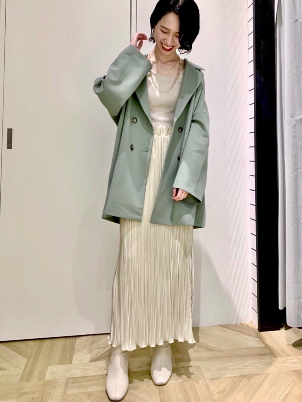 グリーン系のテーラードジャケット、ベージュ系のタンクトップ、ホワイト系のスカートを着用したレディースの春コーディネートの1枚目の写真