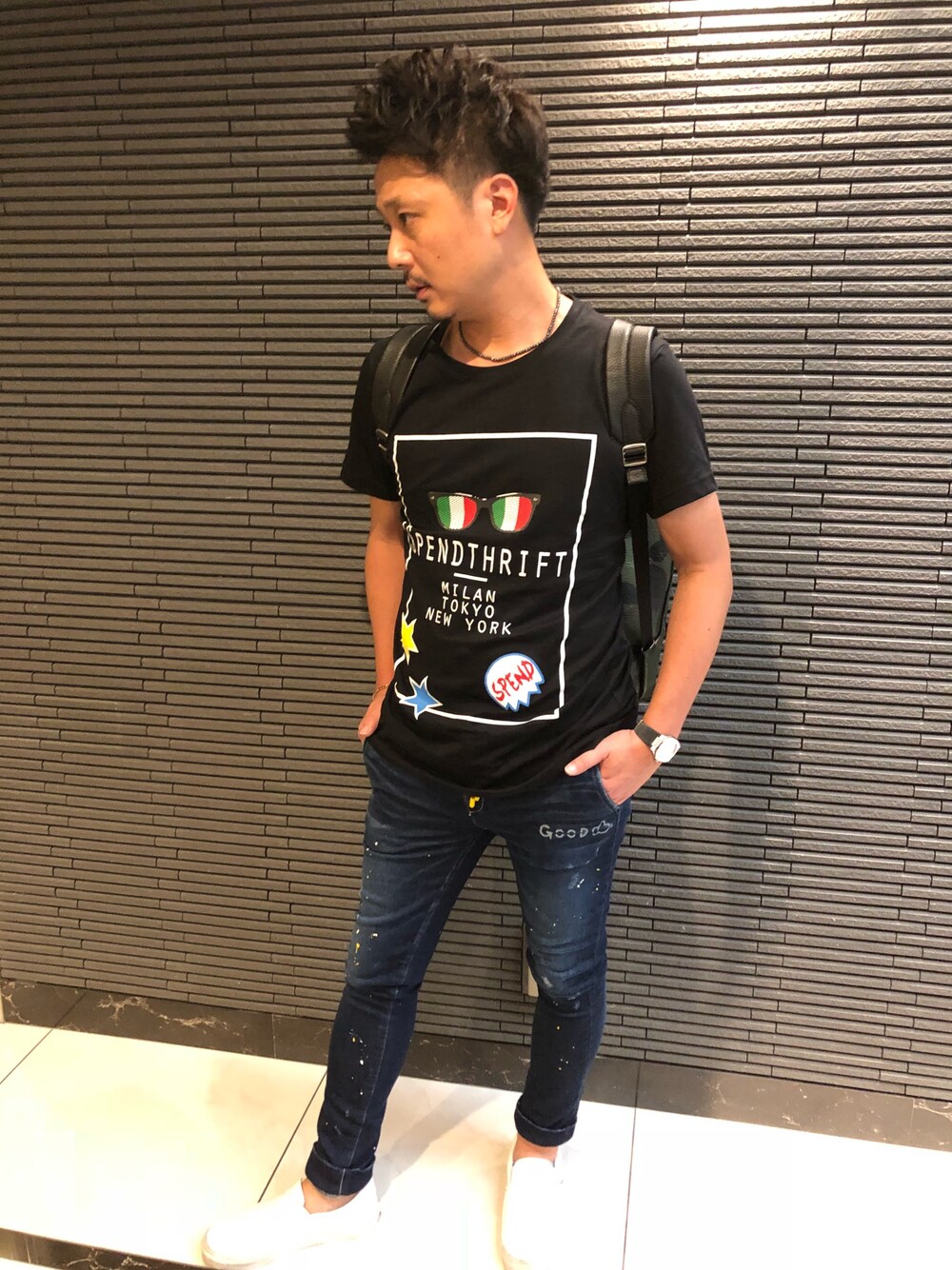 ブラック系のTシャツ/カットソー、ブルー系のデニムパンツ、ホワイト系のスリッポンを着用したメンズの夏コーディネートの1枚目の写真