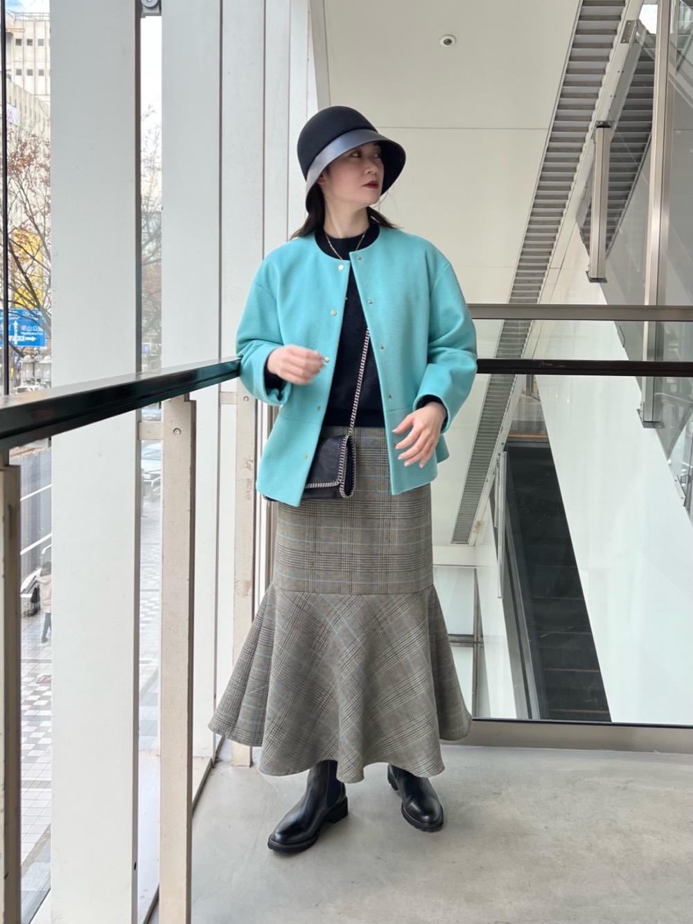 ブラック系のブーツ、グリーン系のノーカラーコート、ブラック系のニット/セーターを着用したレディースの冬コーディネートの1枚目の写真