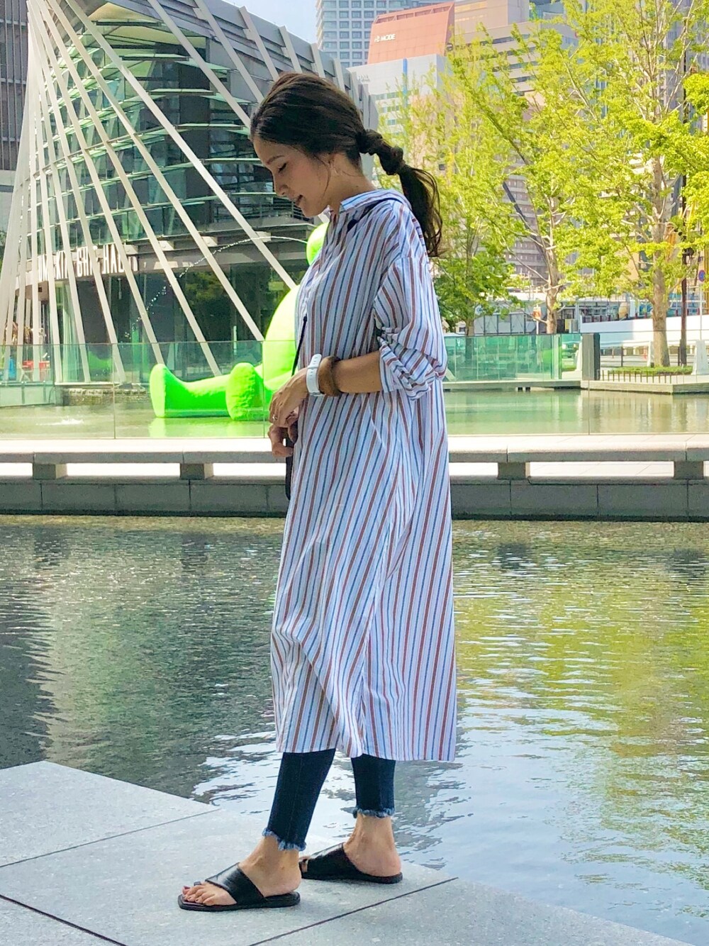 ホワイト系のシャツワンピース、ブルー系のデニムパンツ、ブラック系のサンダルを着用したレディースの夏コーディネートの1枚目の写真