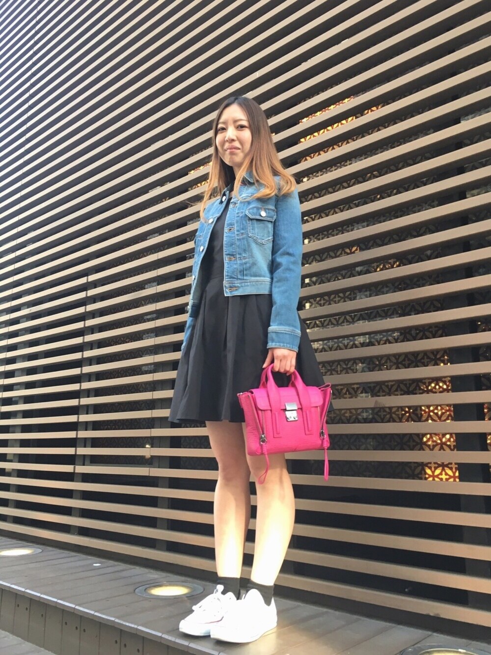 ブルー系のデニムジャケット、ブラック系のワンピース、ピンク系のハンドバッグを着用したレディースの春コーディネートの1枚目の写真