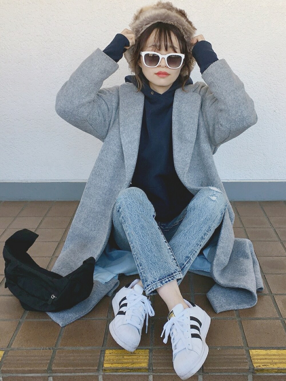 グレー系のチェスターコート、ブルー系のデニムパンツ、ホワイト系のスニーカーを着用したレディースの冬コーディネートの1枚目の写真