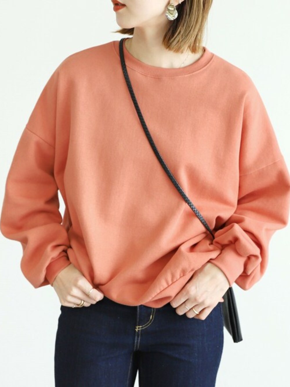 オレンジ系のスウェットを着用したレディースの冬コーディネートの1枚目の写真