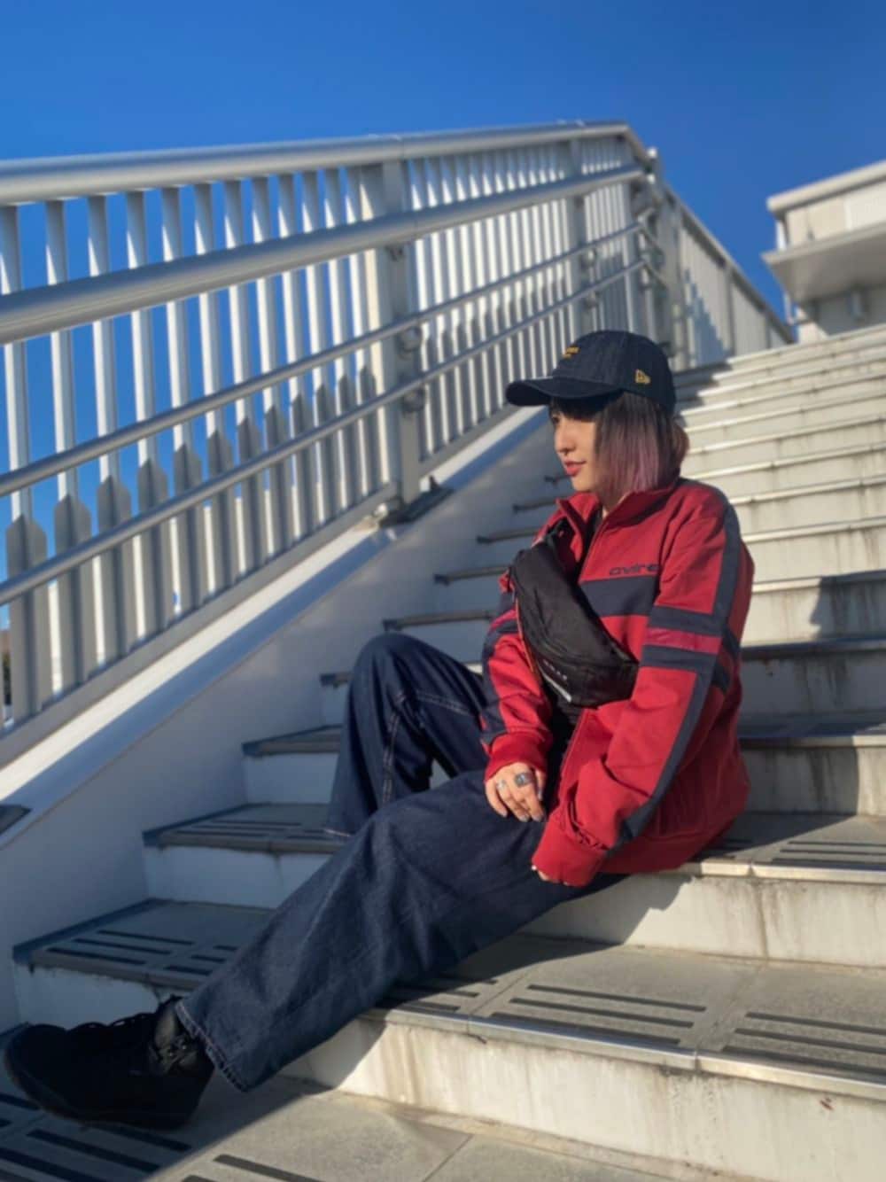 レッド系のジャージ、ブラック系のボディバッグ/ウエストポーチ、ブルー系のキャップを着用したレディースの冬コーディネートの1枚目の写真