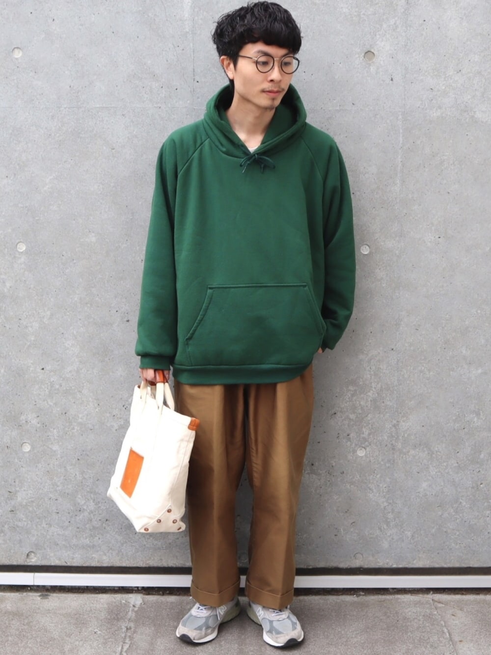 グリーン系のパーカー、ブラウン系のパンツ、ベージュ系のトートバッグを着用したメンズの春コーディネートの1枚目の写真