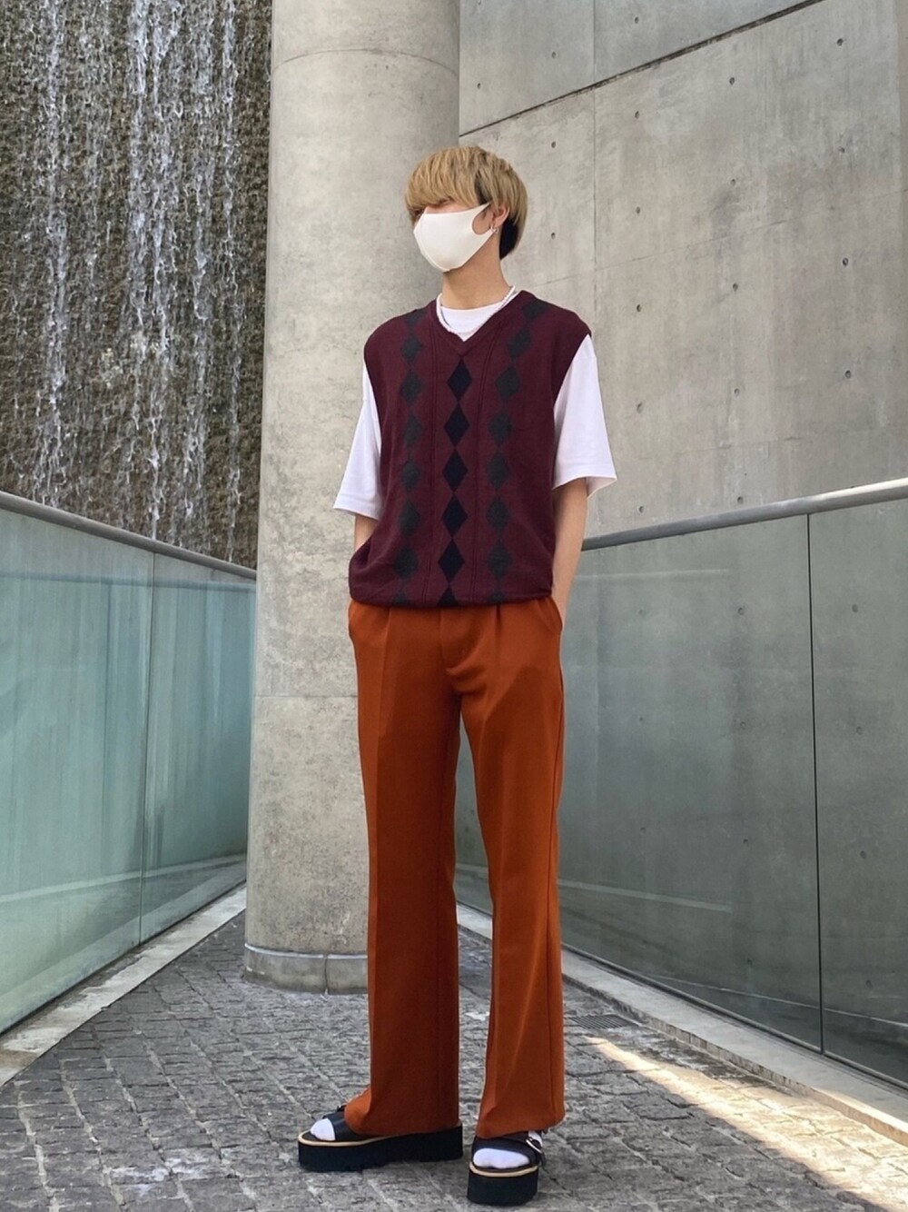 レッド系のベスト、ホワイト系のTシャツ/カットソー、オレンジ系のスラックスを着用したメンズの夏コーディネートの1枚目の写真