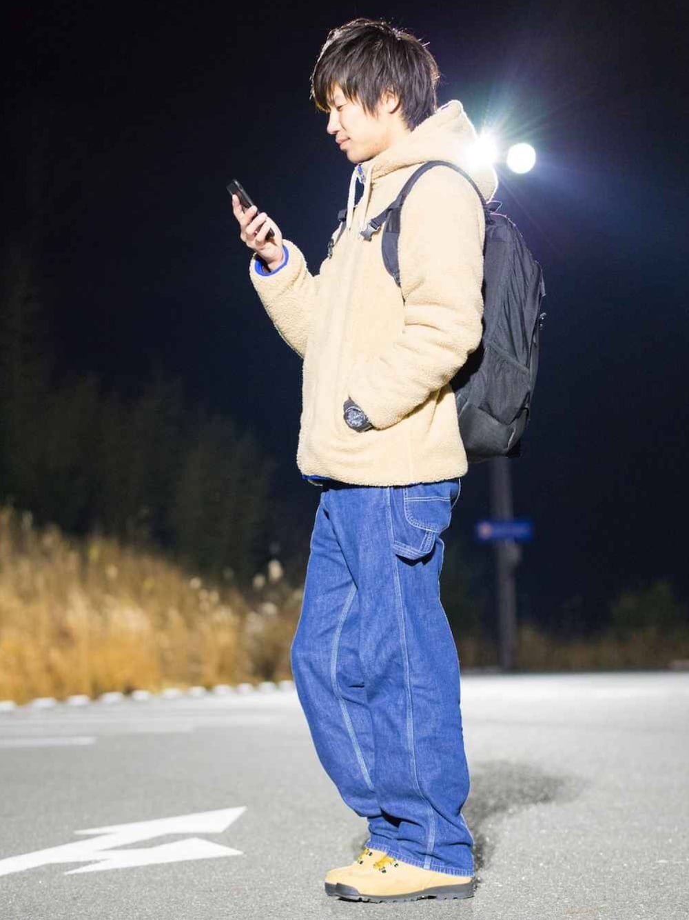 イエロー系のブルゾン、ブラック系のバックパック/リュック、ブルー系のデニムパンツを着用したメンズの冬コーディネートの1枚目の写真