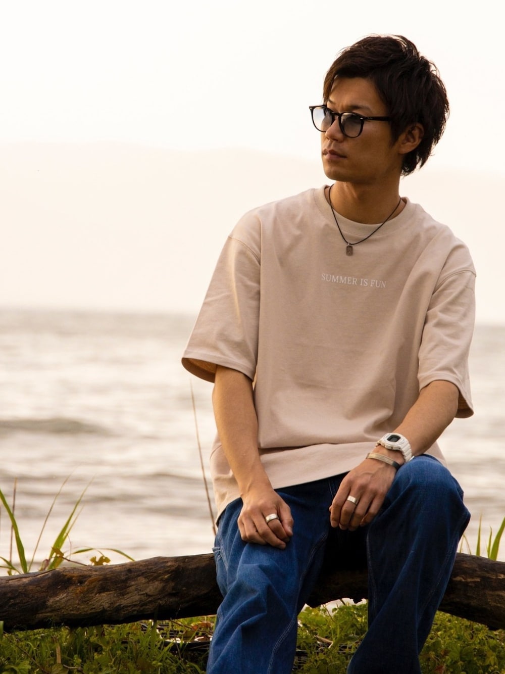 ベージュ系のTシャツ/カットソー、ブルー系のデニムパンツ、ブラック系のサングラスを着用したメンズの夏コーディネートの1枚目の写真