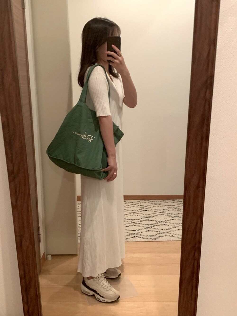 グリーン系のトートバッグ、ホワイト系のワンピース、ベージュ系のスニーカーを着用したレディースの秋コーディネートの1枚目の写真