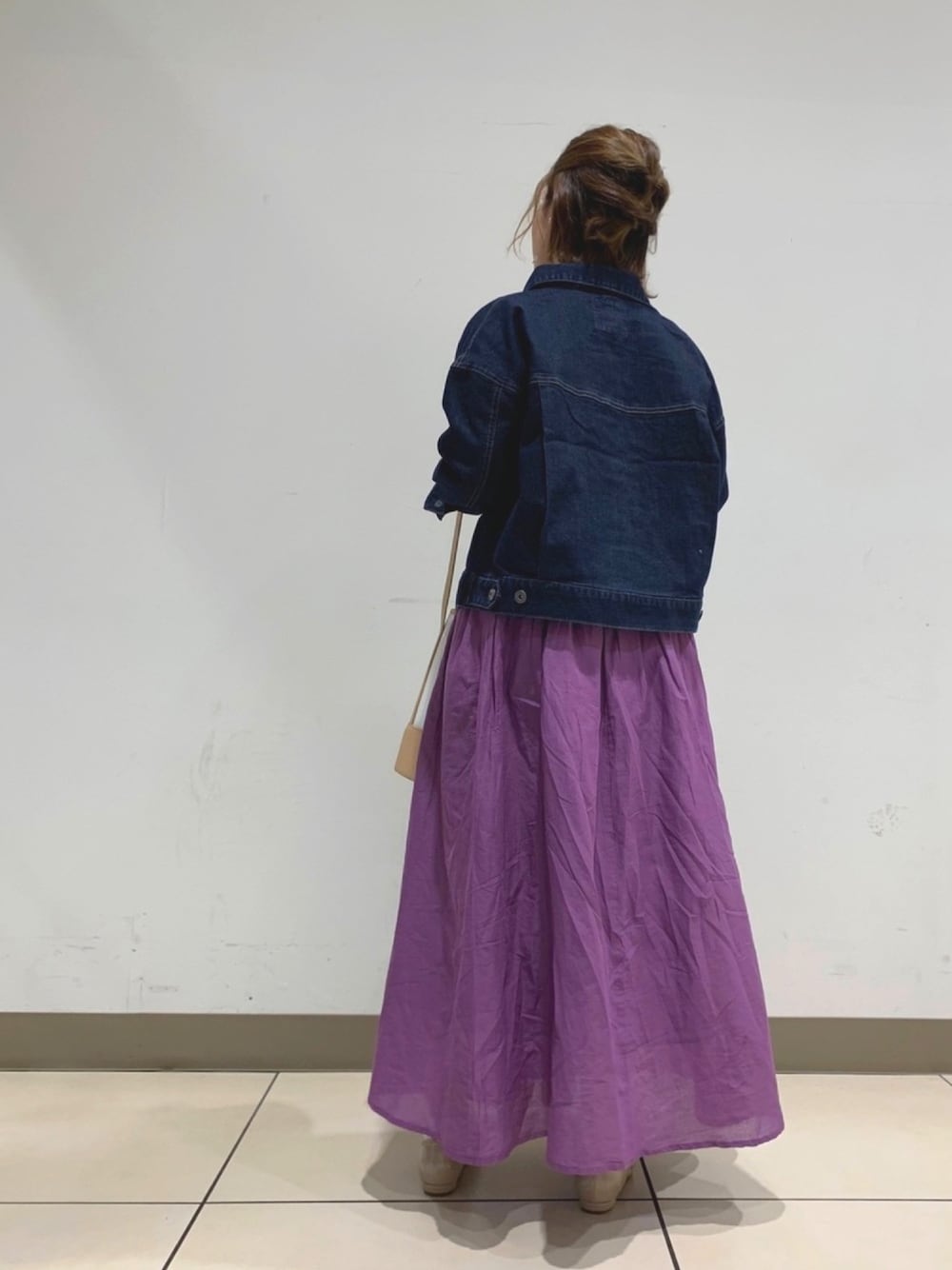 ブルー系のデニムジャケット、パープル系のスカート、ベージュ系のショルダーバッグを着用したレディースの春コーディネートの1枚目の写真