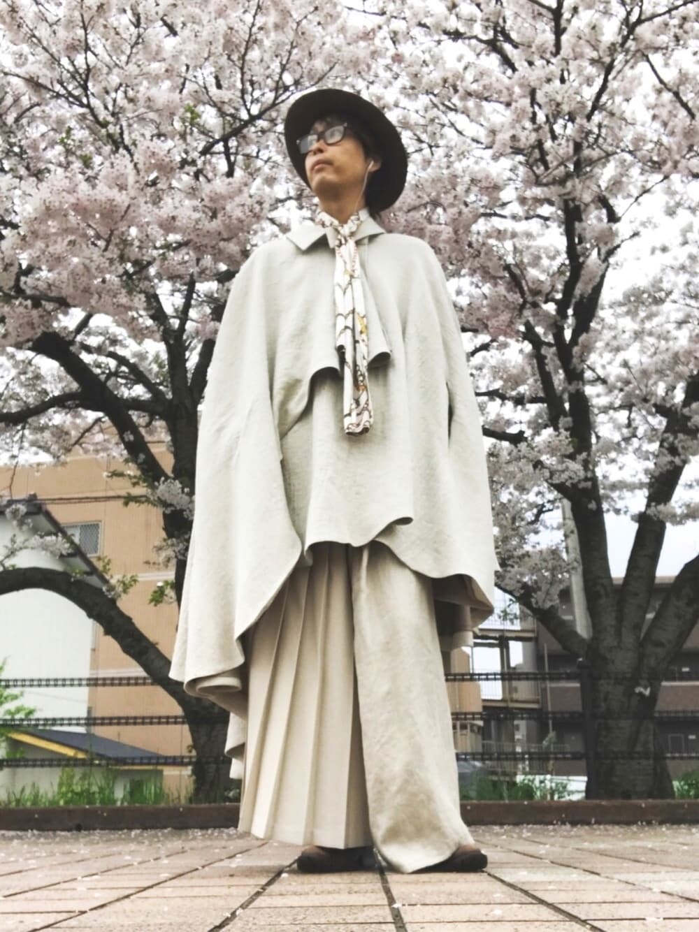 ベージュ系のポンチョ、ベージュ系のパンツ、ブラウン系のブーツを着用したメンズの春コーディネートの1枚目の写真