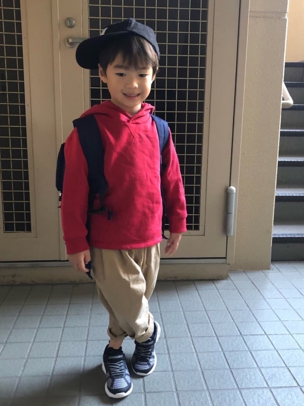 レッド系のパーカー、ベージュ系のその他パンツ、ブラック系のスニーカーを着用したキッズの秋コーディネートの1枚目の写真