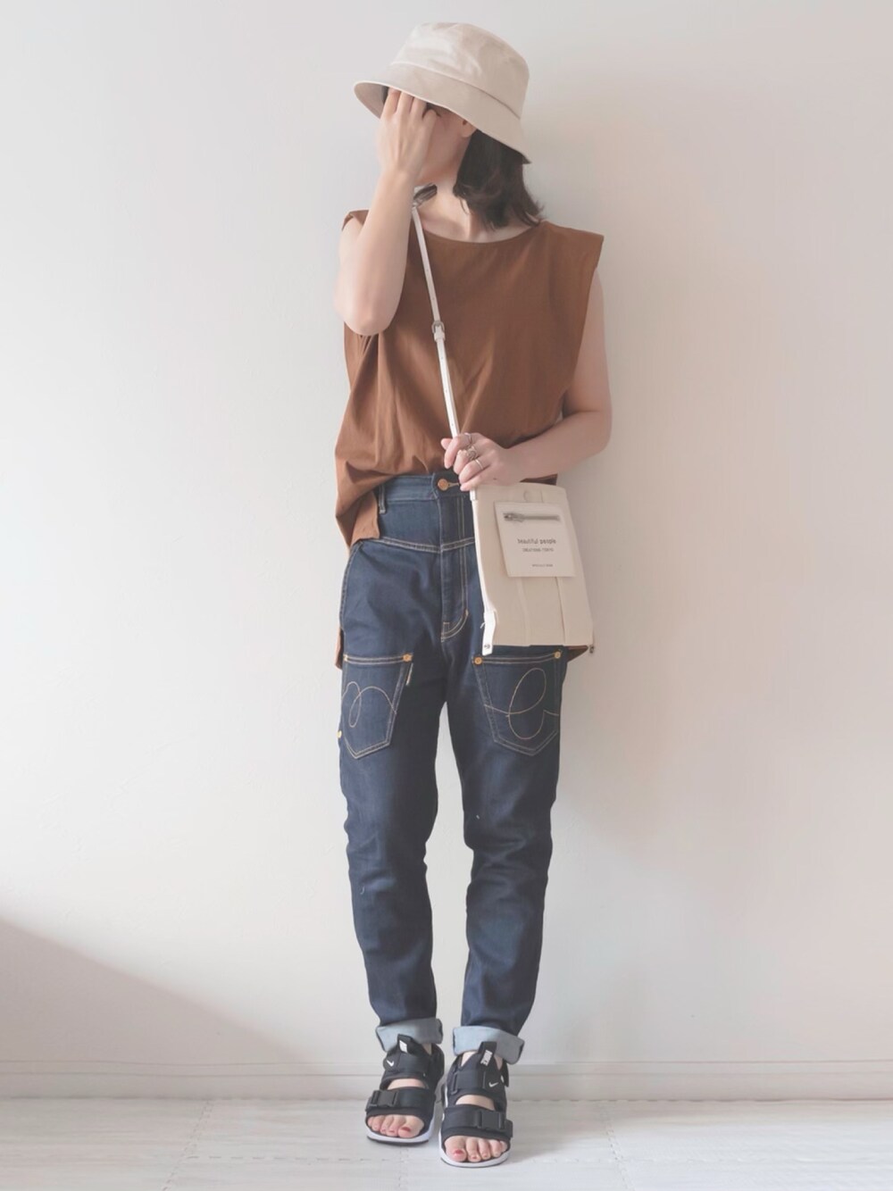 ブラウン系のタンクトップ、ホワイト系のショルダーバッグ、ブルー系のデニムパンツを着用したレディースの夏コーディネートの1枚目の写真