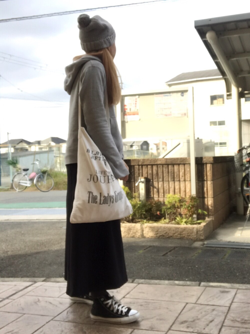 グレー系のパーカー、ホワイト系のトートバッグ、ブラック系のスカートを着用したレディースの冬コーディネートの1枚目の写真