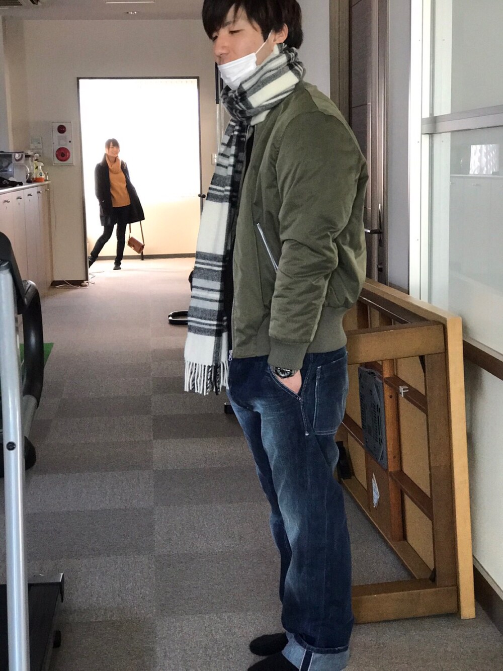 グリーン系のミリタリージャケット、ブルー系のデニムパンツ、ホワイト系のマフラーを着用したメンズの冬コーディネートの1枚目の写真