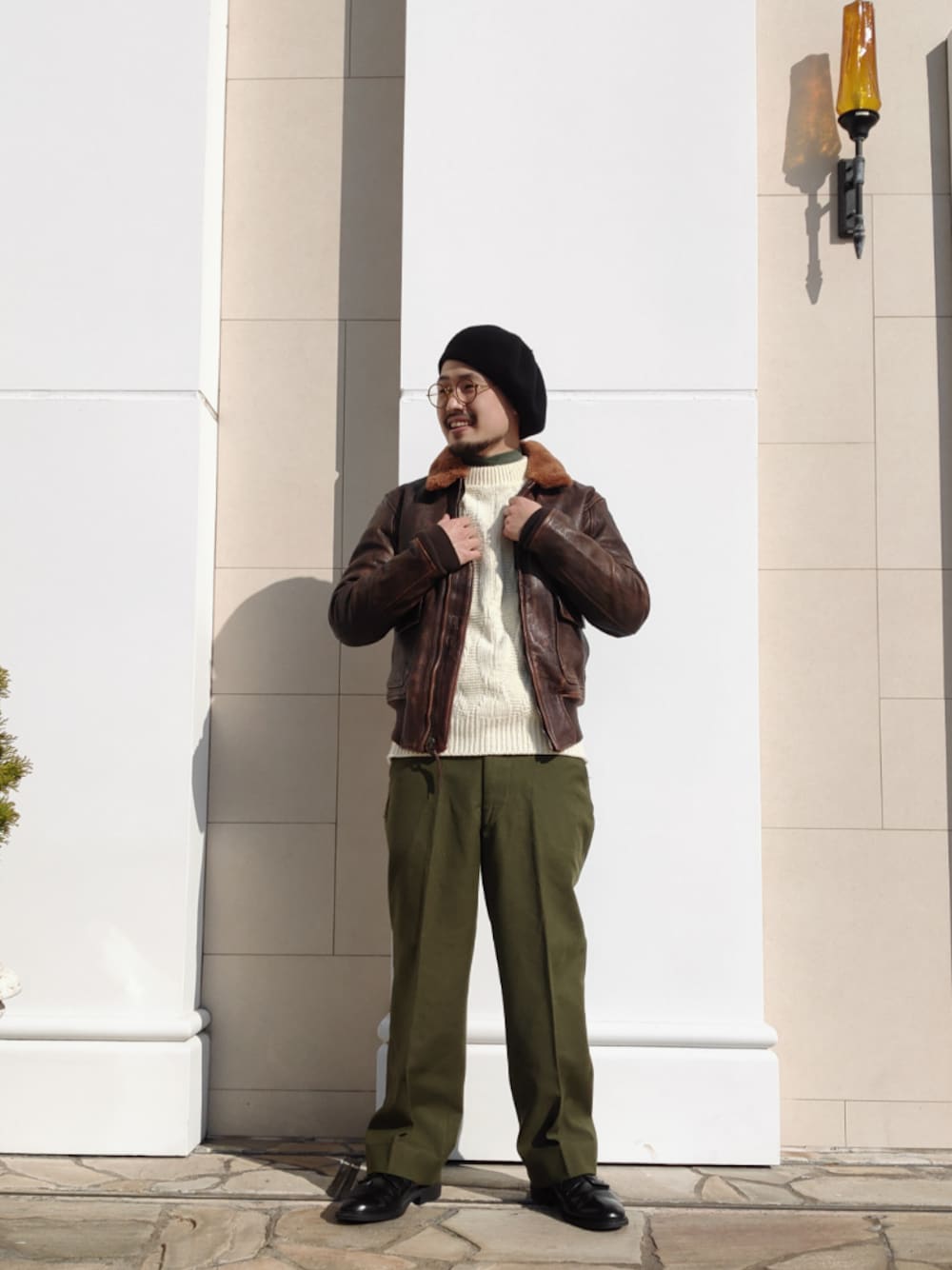 ブラウン系のミリタリージャケット、グリーン系のスラックス、ブラック系のドレスシューズを着用したメンズの冬コーディネートの1枚目の写真