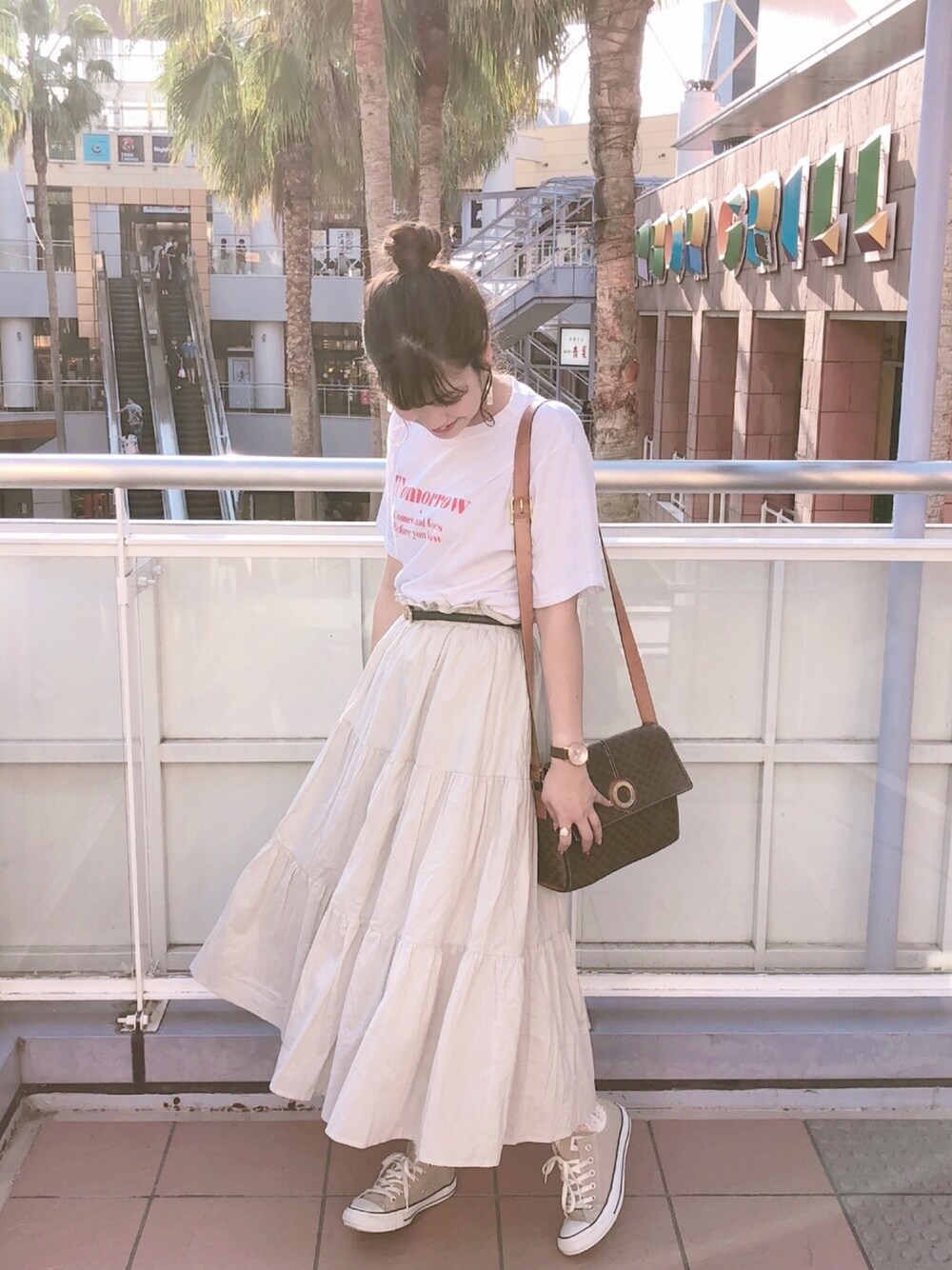 グレー系のスカート、ベージュ系のスニーカー、ブラウン系のバッグを着用したレディースの夏コーディネートの1枚目の写真