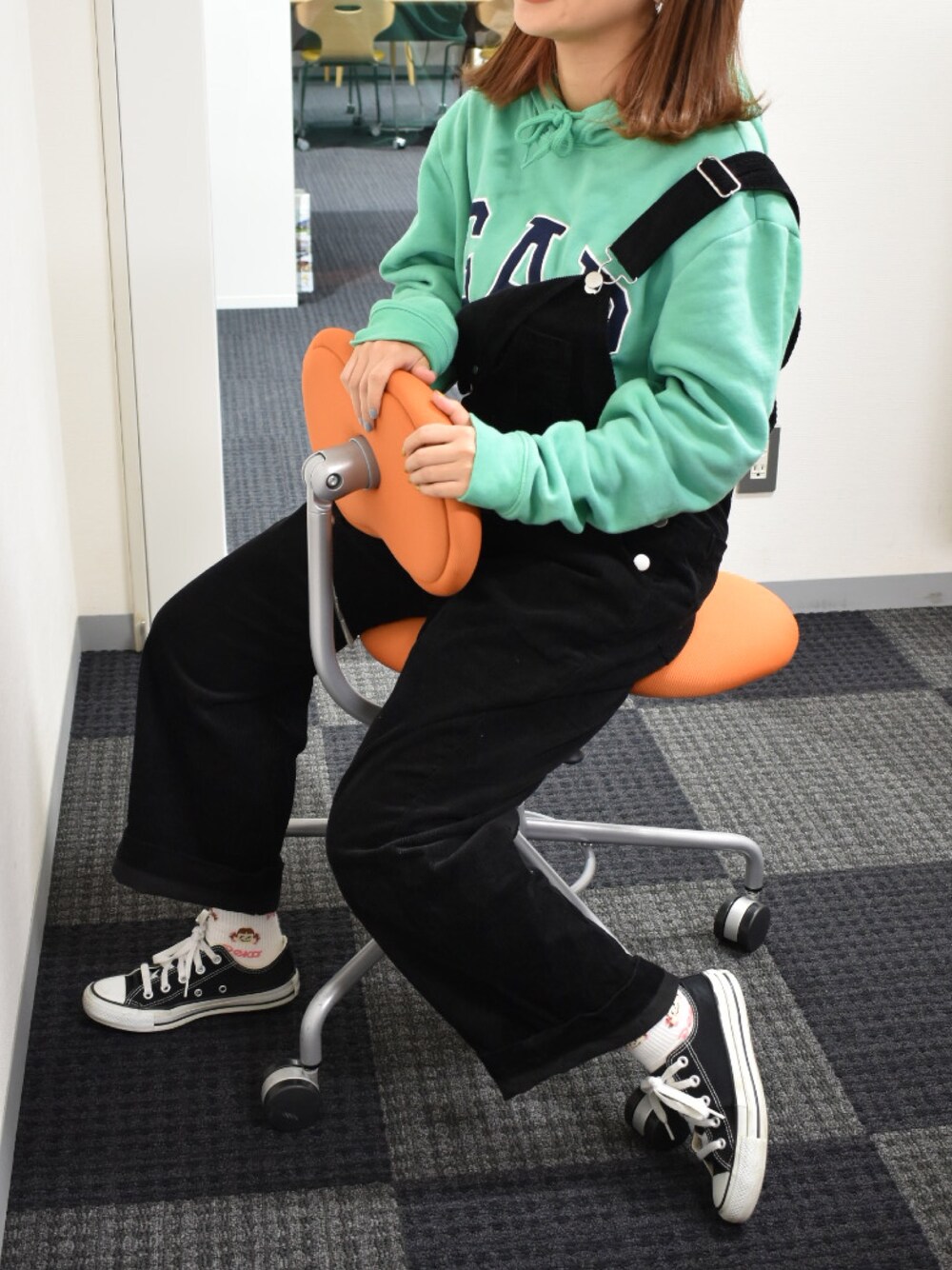 グリーン系のパーカー、ブラック系のサロペット/オーバーオール、ブラック系のスニーカーを着用したレディースの秋コーディネートの1枚目の写真