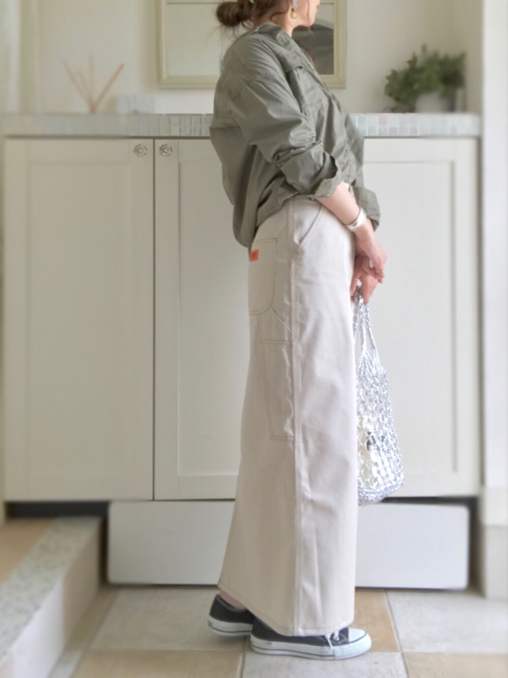 ベージュ系のスカート、シルバー系のかごバッグ、ブラック系のスニーカーを着用したレディースの春コーディネートの1枚目の写真