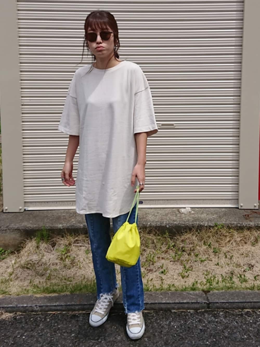 ブルー系のデニムパンツ、ベージュ系のスニーカー、グリーン系のピアス（両耳用）を着用したレディースの春コーディネートの1枚目の写真