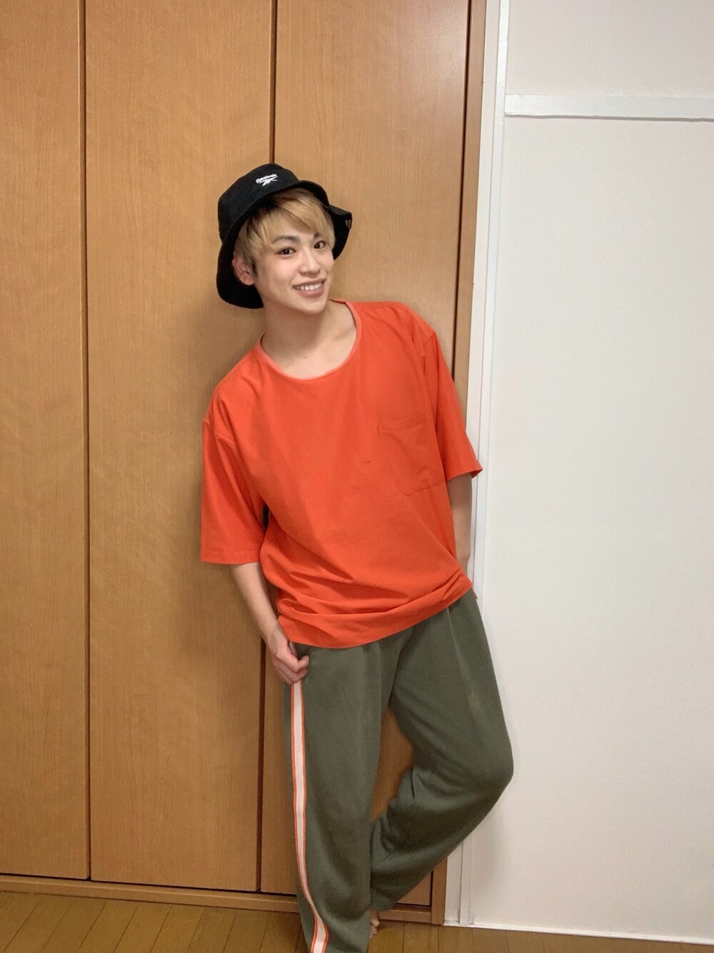 オレンジ系のTシャツ/カットソー、グリーン系のパンツ、ブラック系のハットを着用したメンズの夏コーディネートの1枚目の写真